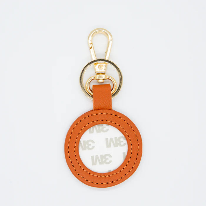 Round orange leather keychain with gold clasp on a light gray background